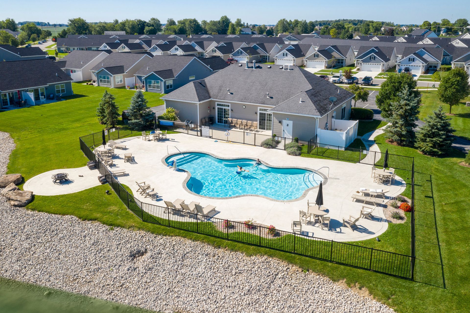 Aerial view of a swimming pool with lounge chairs, a large house, and surrounding houses in a neighborhood.