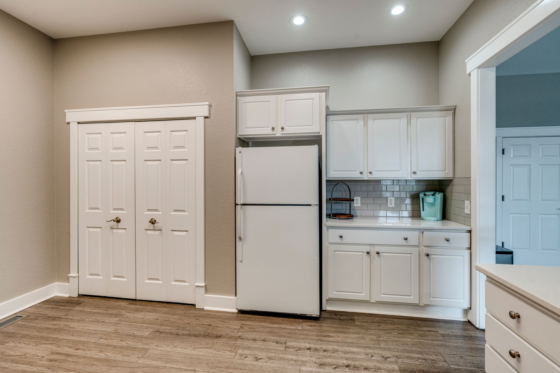 Kitchen area with white cabinets, refrigerator, and closed closet doors. Light walls and flooring.