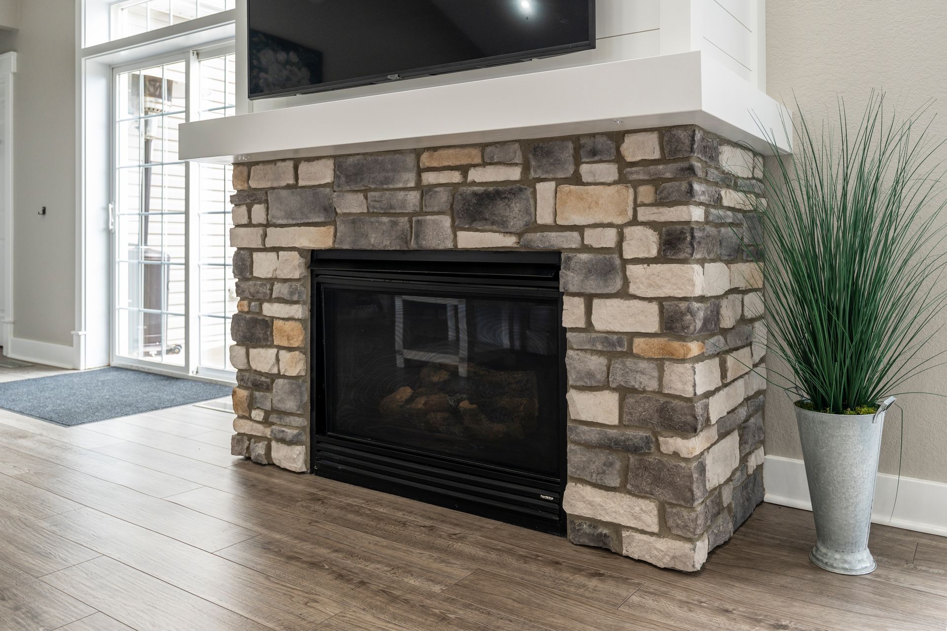 Stone fireplace with TV above, next to a potted plant, with sliding glass door in background.