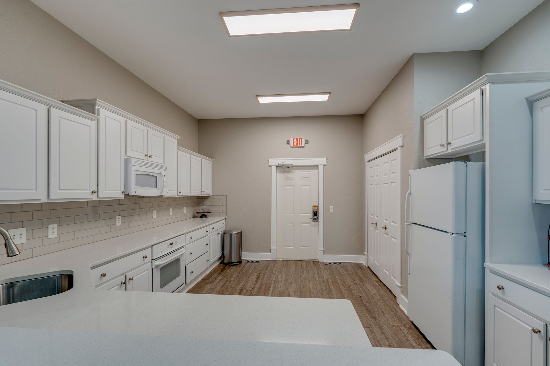 White kitchen with cabinets, appliances, and a countertop. Doorway leads to a hallway.
