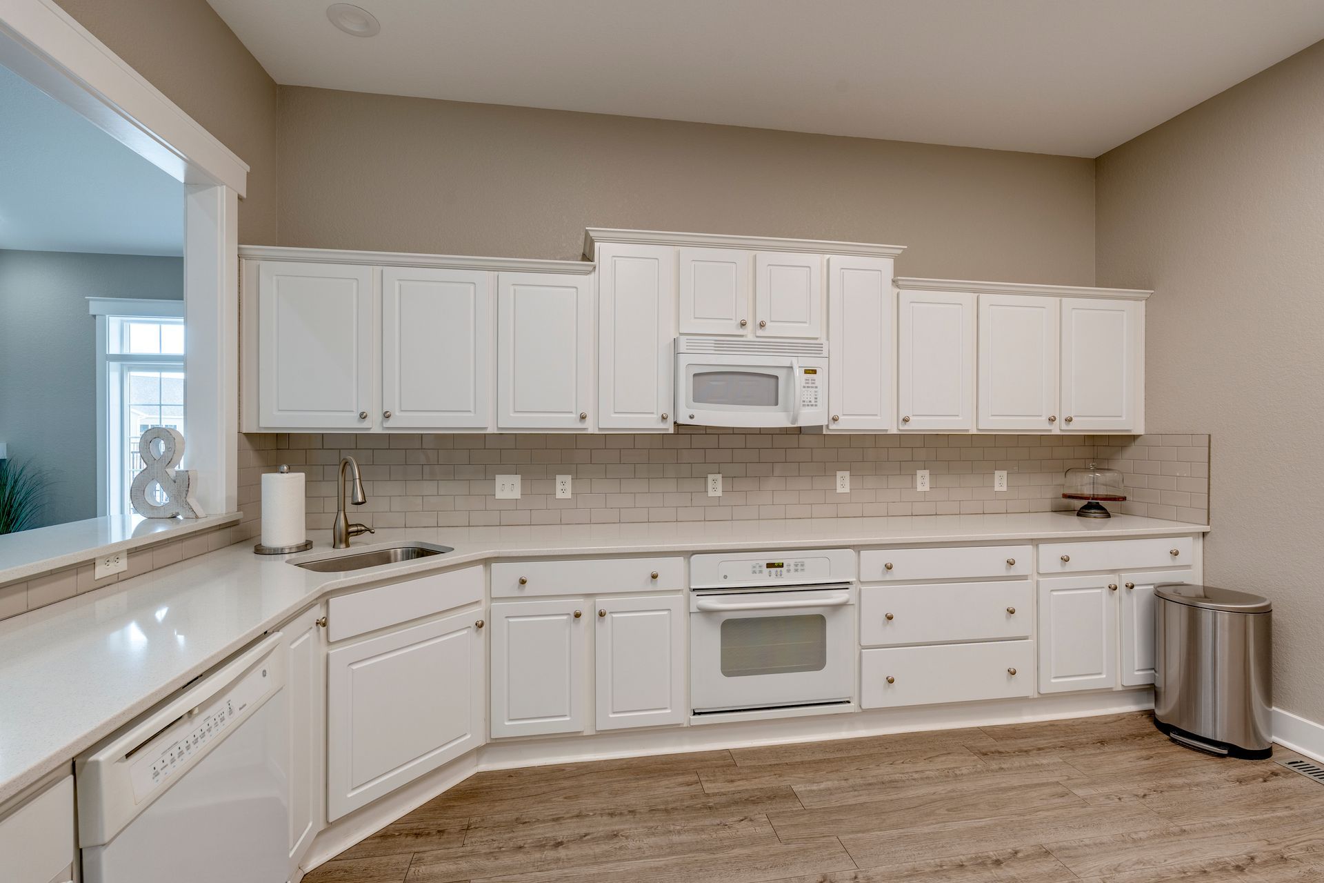 White kitchen with cabinets, appliances, light-colored countertops, and a window.