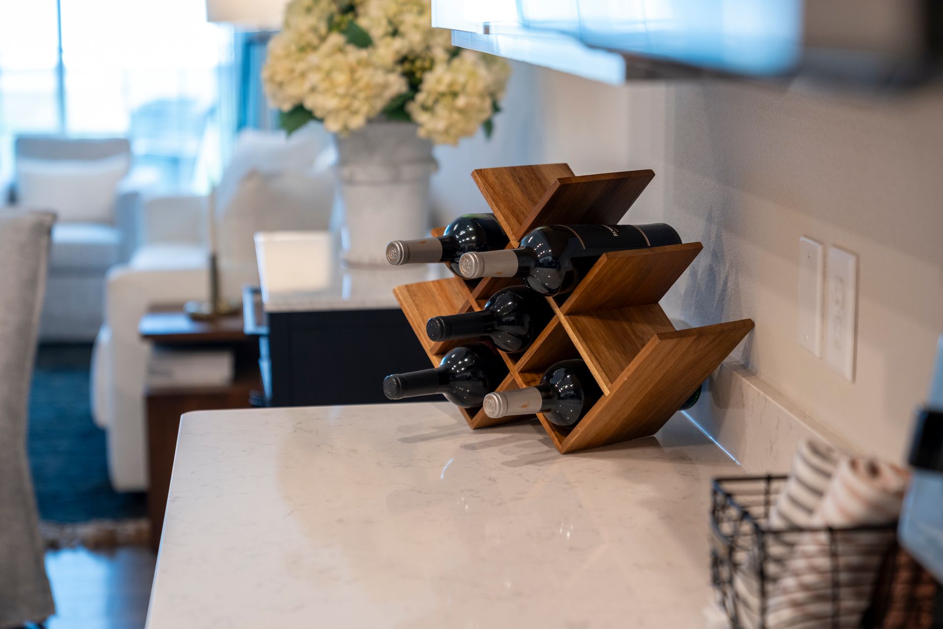 Wooden wine rack on a marble countertop with wine bottles; flowers in the background.