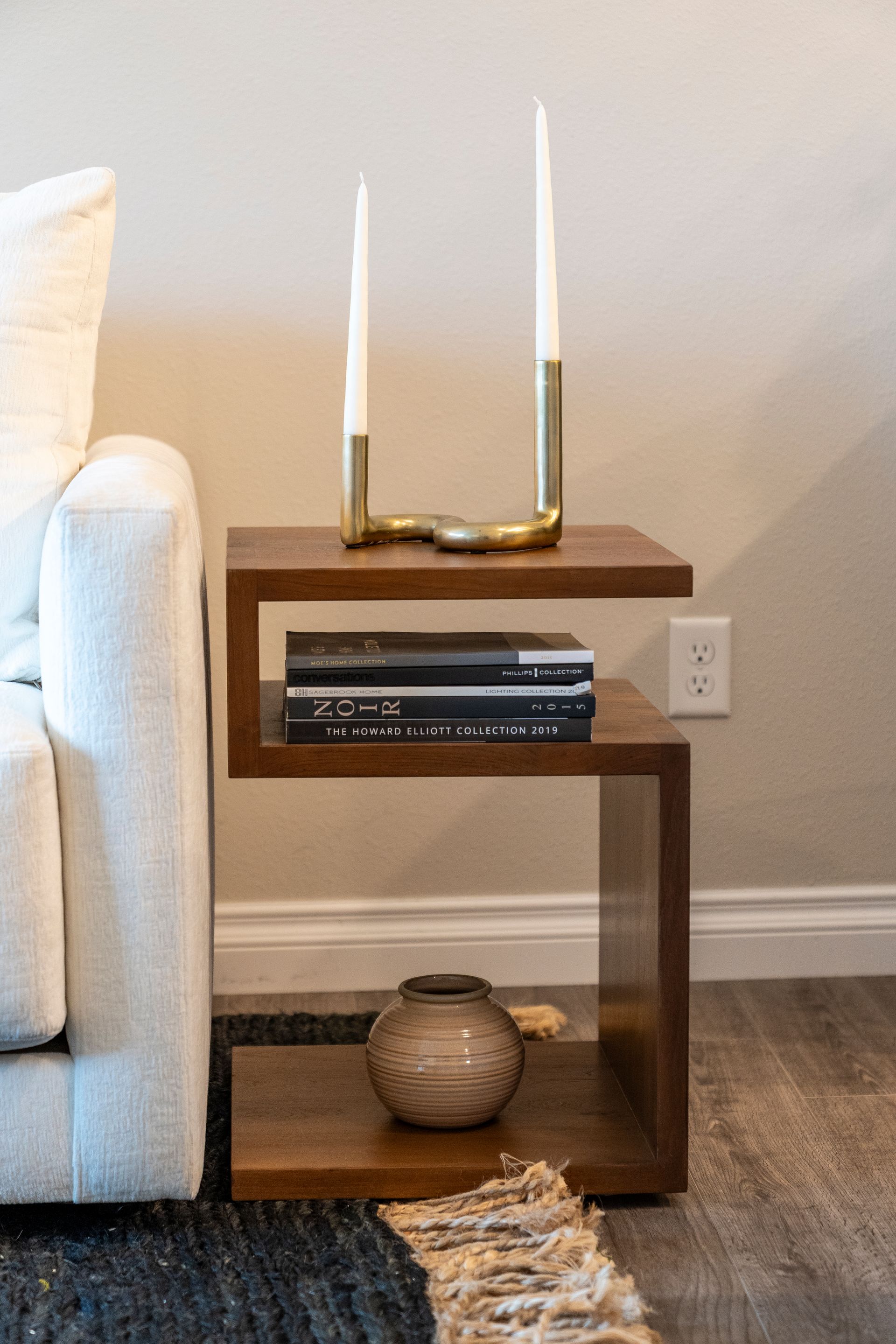 Wooden side table with books and candles next to a white couch.