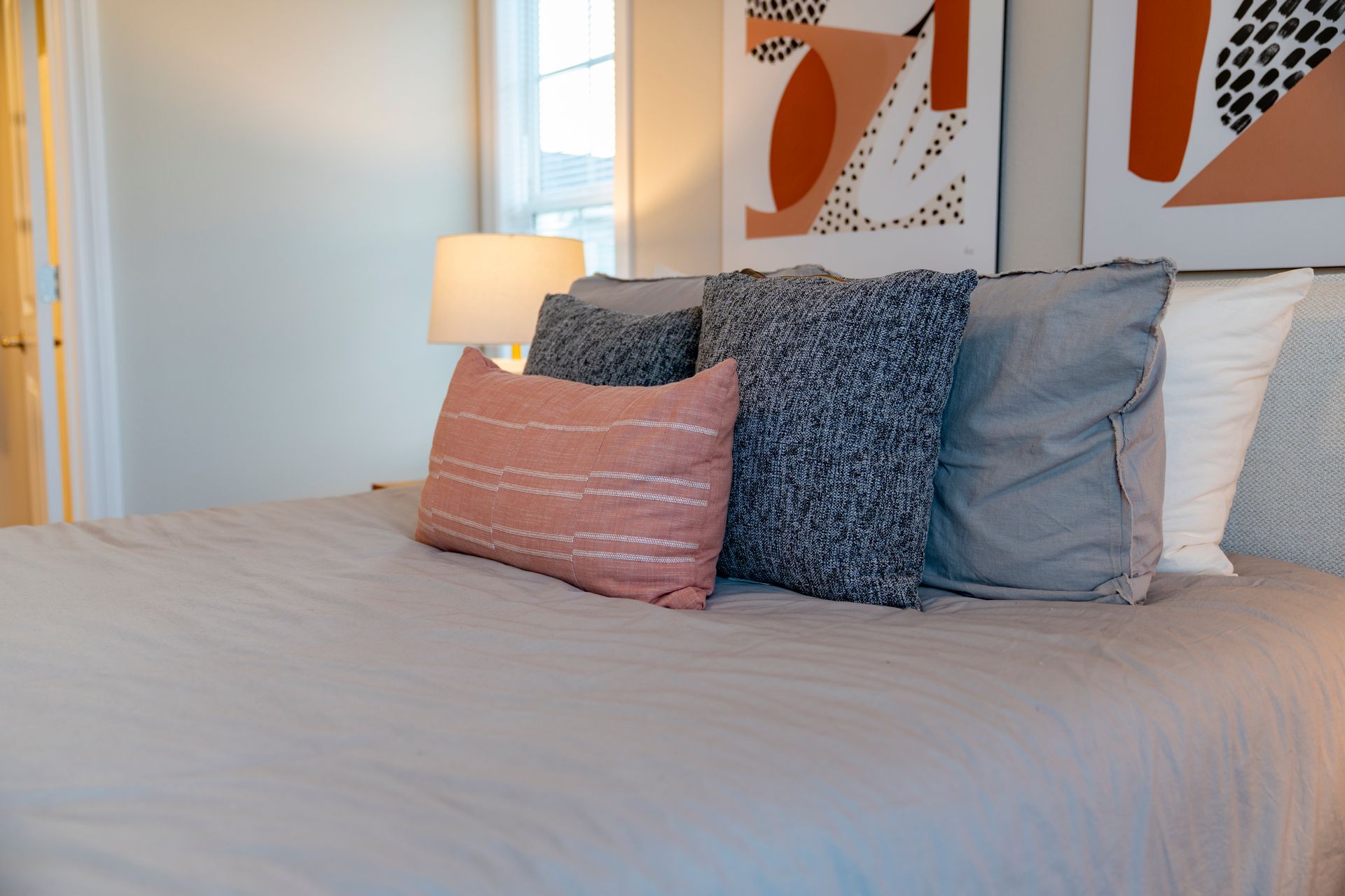 Bed with gray linens and decorative pillows in front of a window.