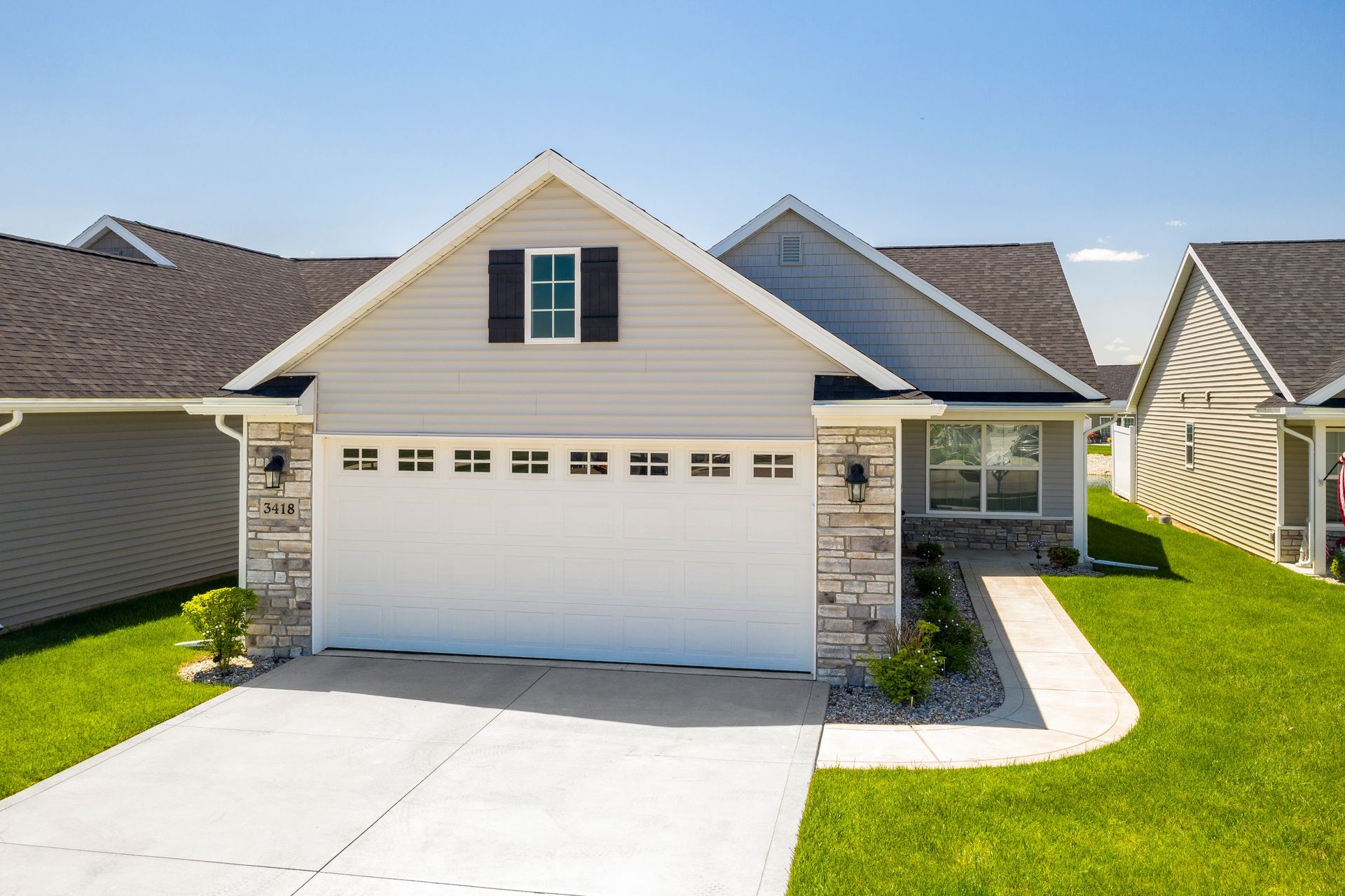 Gray and white house with a two-car garage, stone accents, and a green lawn on a sunny day.