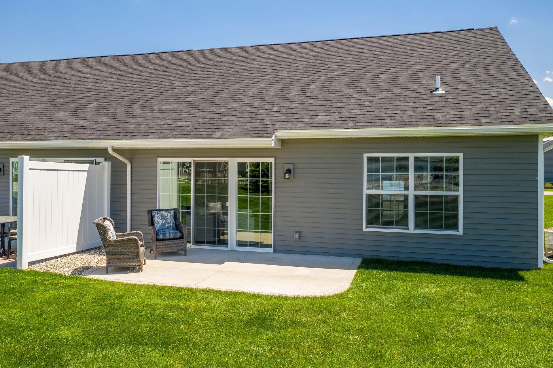 Backyard patio with gray siding, sliding glass door, and window. Lawn and a gray roof are visible.
