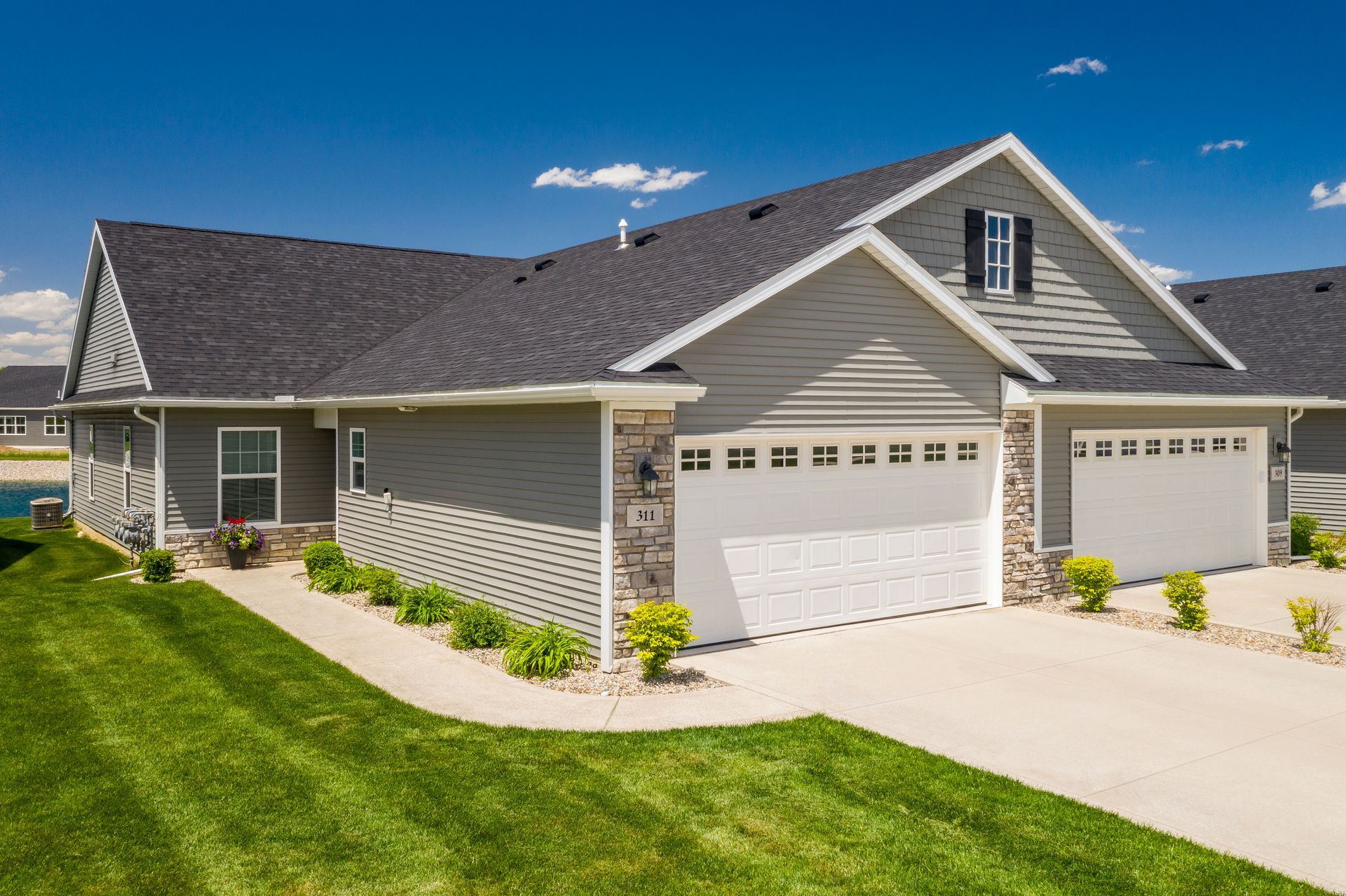 Gray house with two-car garage, green lawn, and blue sky.