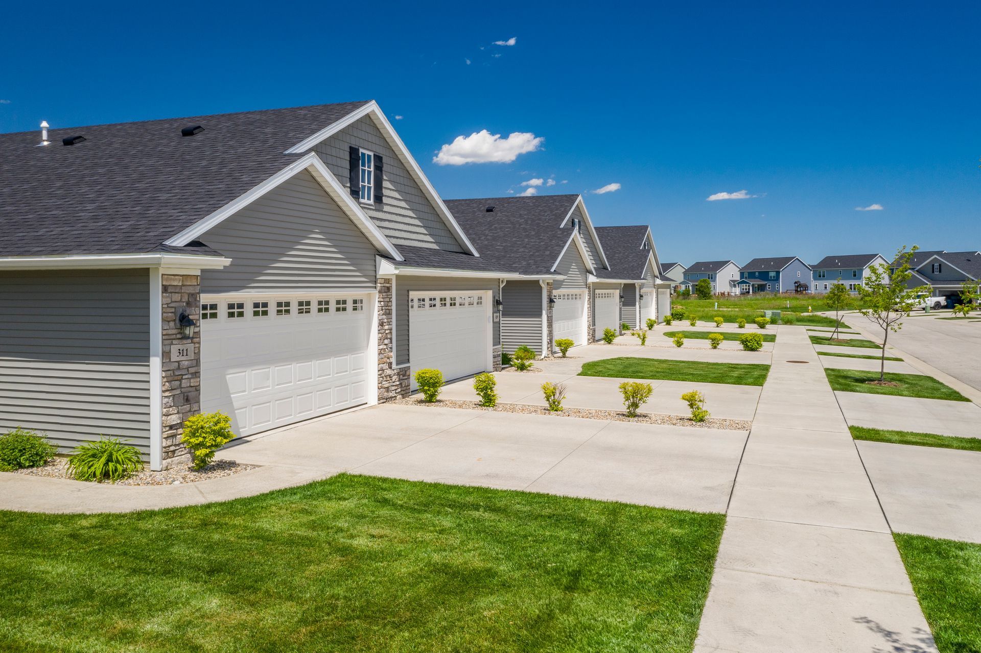 Row of gray houses with white garage doors and green lawns, sunny day.