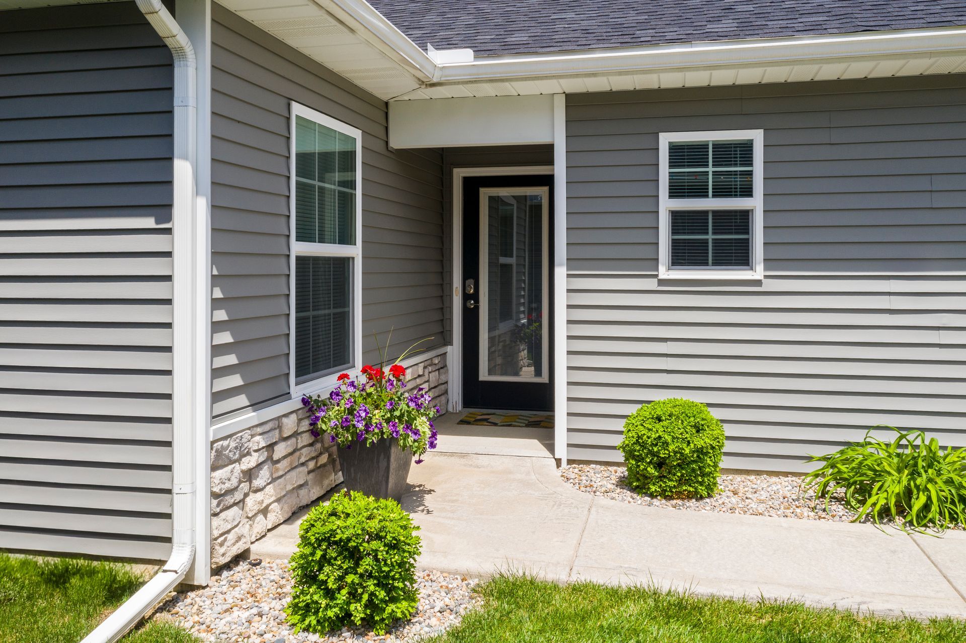 Gray house entrance with windows, bushes, and a flower pot.