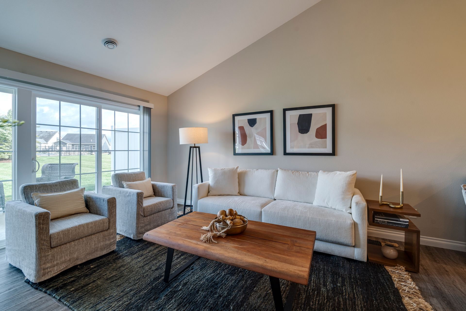 Living room with white sofa, armchairs, coffee table, rug, and window overlooking a yard.