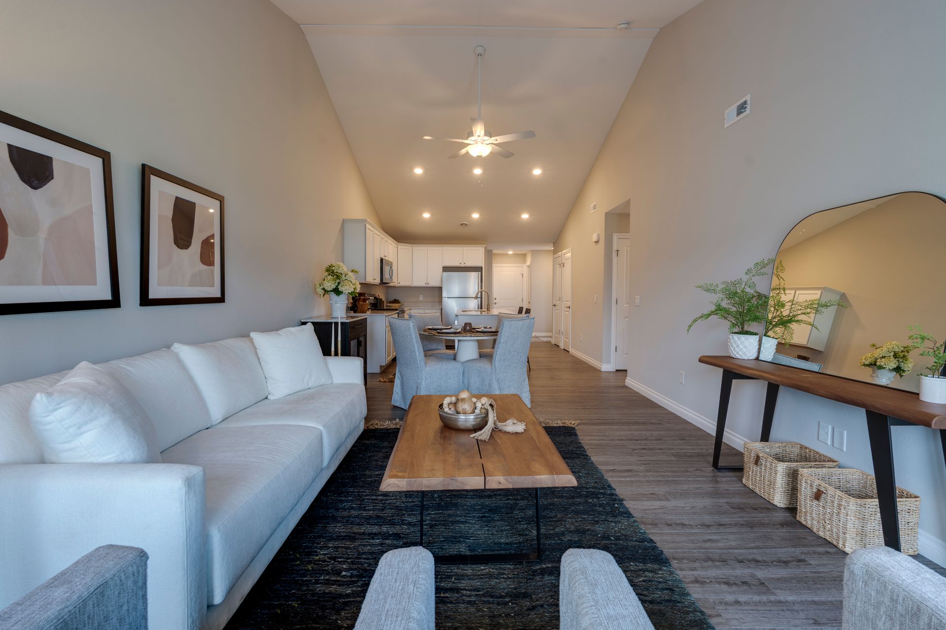 Spacious, modern living room with white couch, wooden coffee table, and open kitchen.