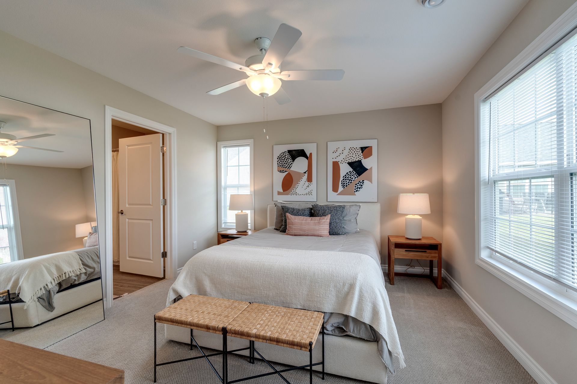 Bedroom with bed, bench, artwork, windows, and ceiling fan.