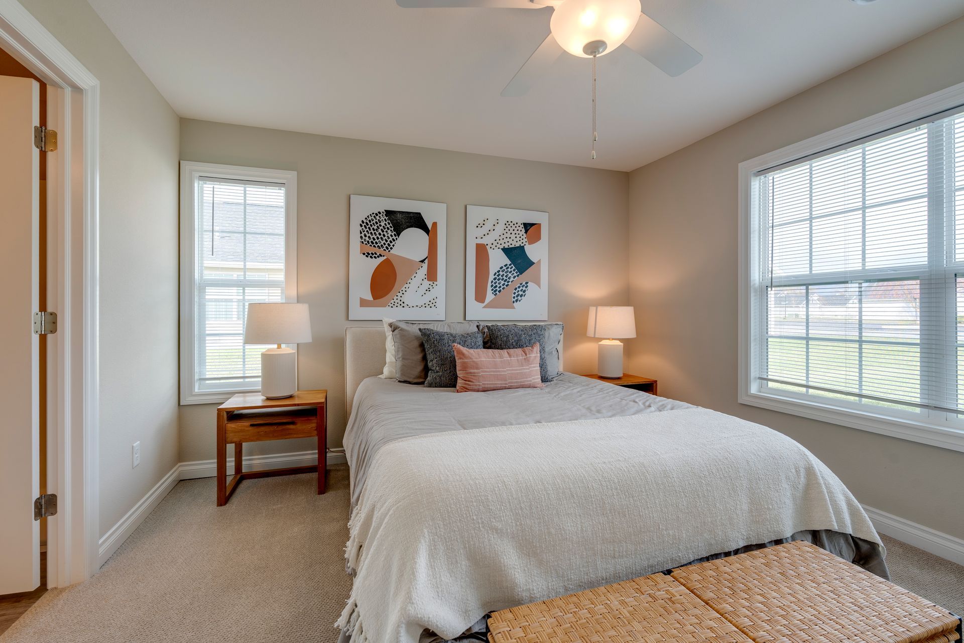 Bedroom with bed, nightstands, windows, and abstract art on the wall. Neutral colors, natural light.