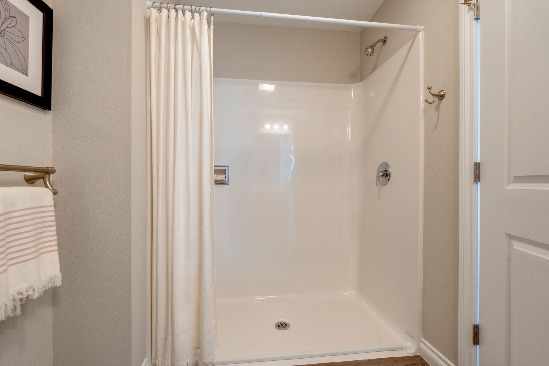 White shower stall in a bathroom with beige walls, cream shower curtain, and a towel.