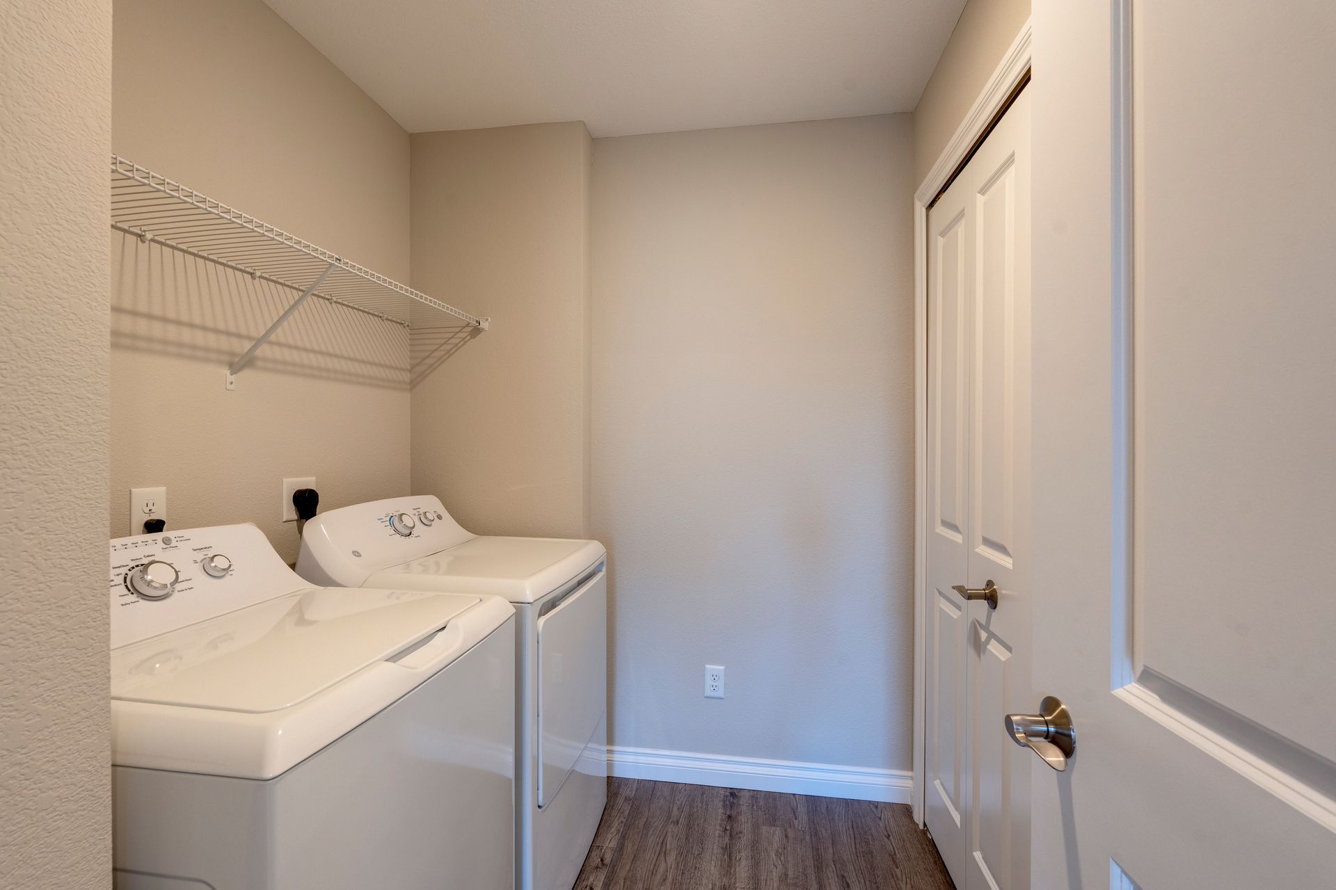 Laundry room with white washer and dryer, wire shelving, and a closed white door.