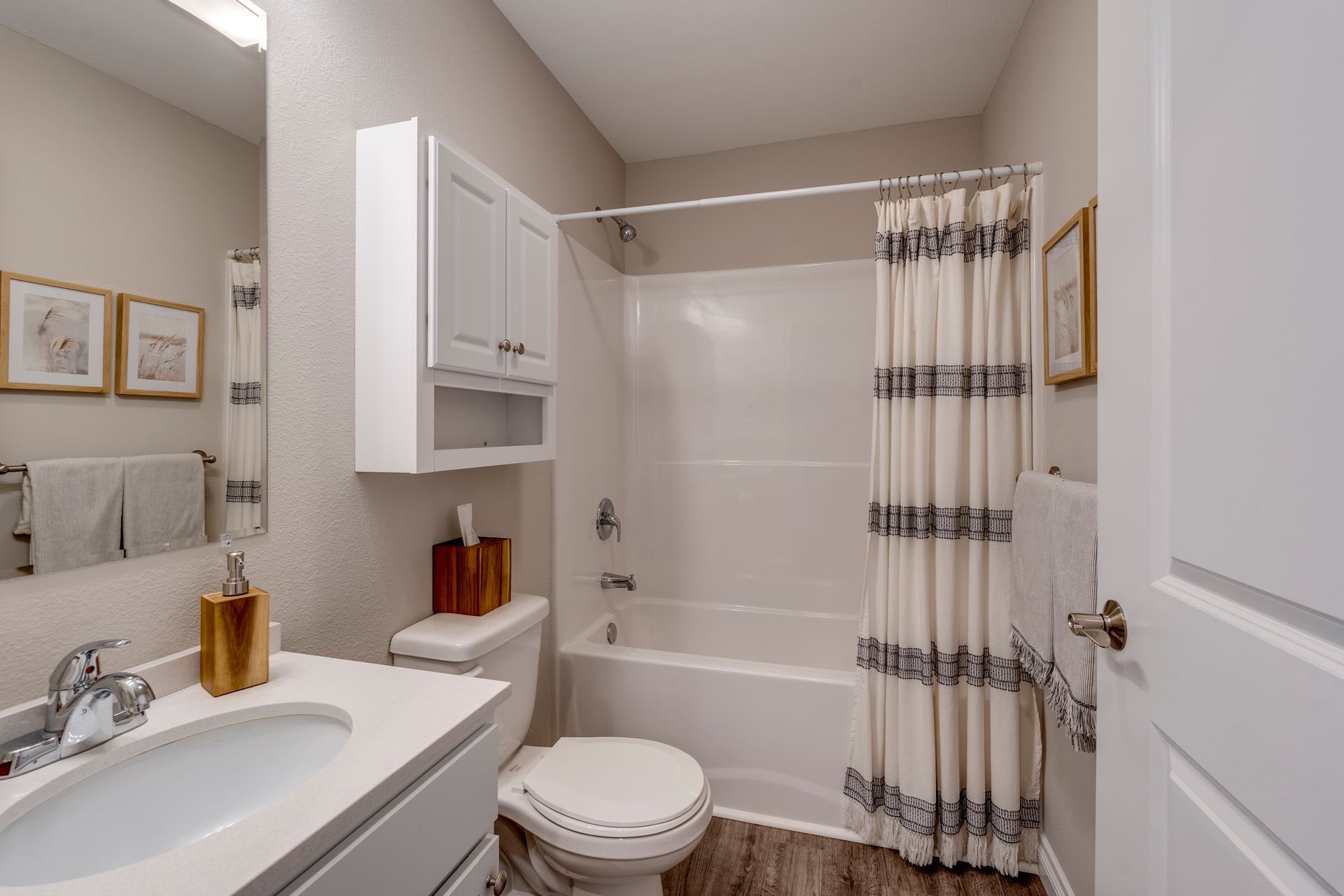 Bathroom with white sink, toilet, tub, and neutral color walls. Decorative framed art hangs on wall.