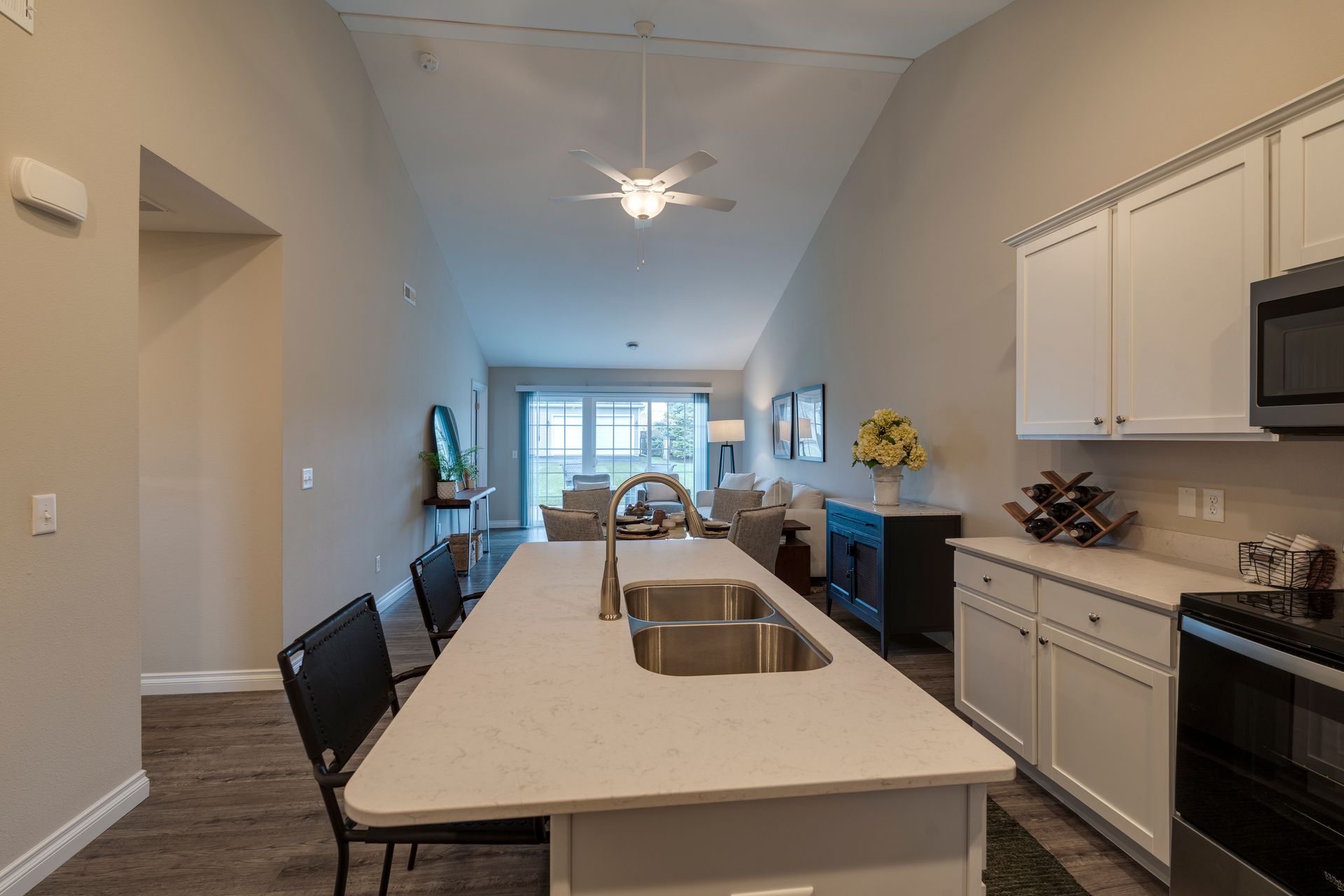 Modern kitchen with island, cabinets, and appliances; leads to living area with furniture and balcony.