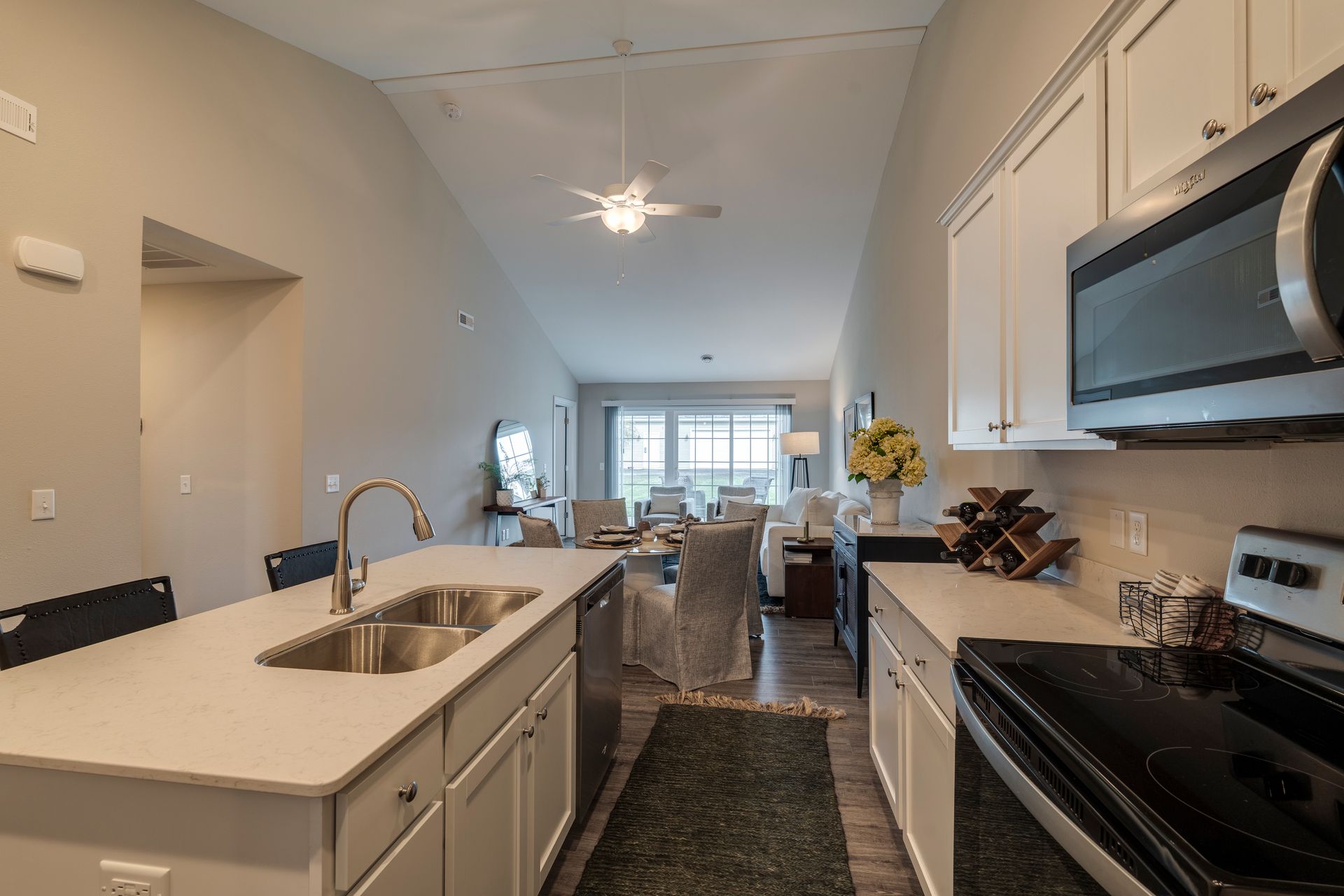 Kitchen with white cabinets, island with sink, and view into living area with table and couch.