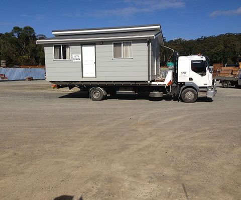 A Truck Carrying A Portable House — DJ’s Tilt Tray Service in Urunga NSW