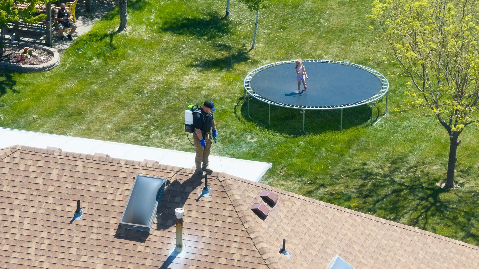 An aerial view of a man spraying a trampoline in a backyard.