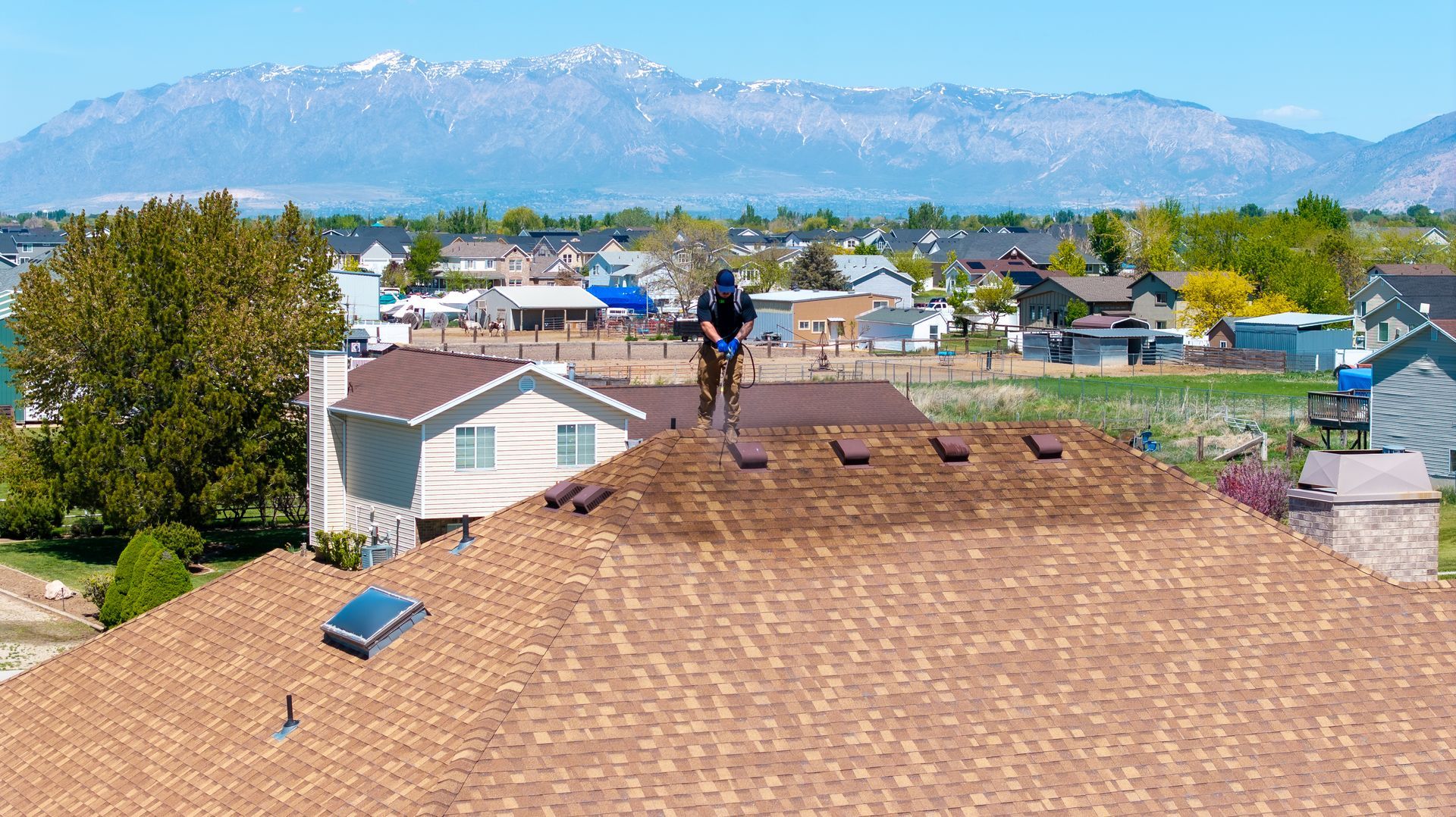 A man is working on the roof of a house with mountains in the background.