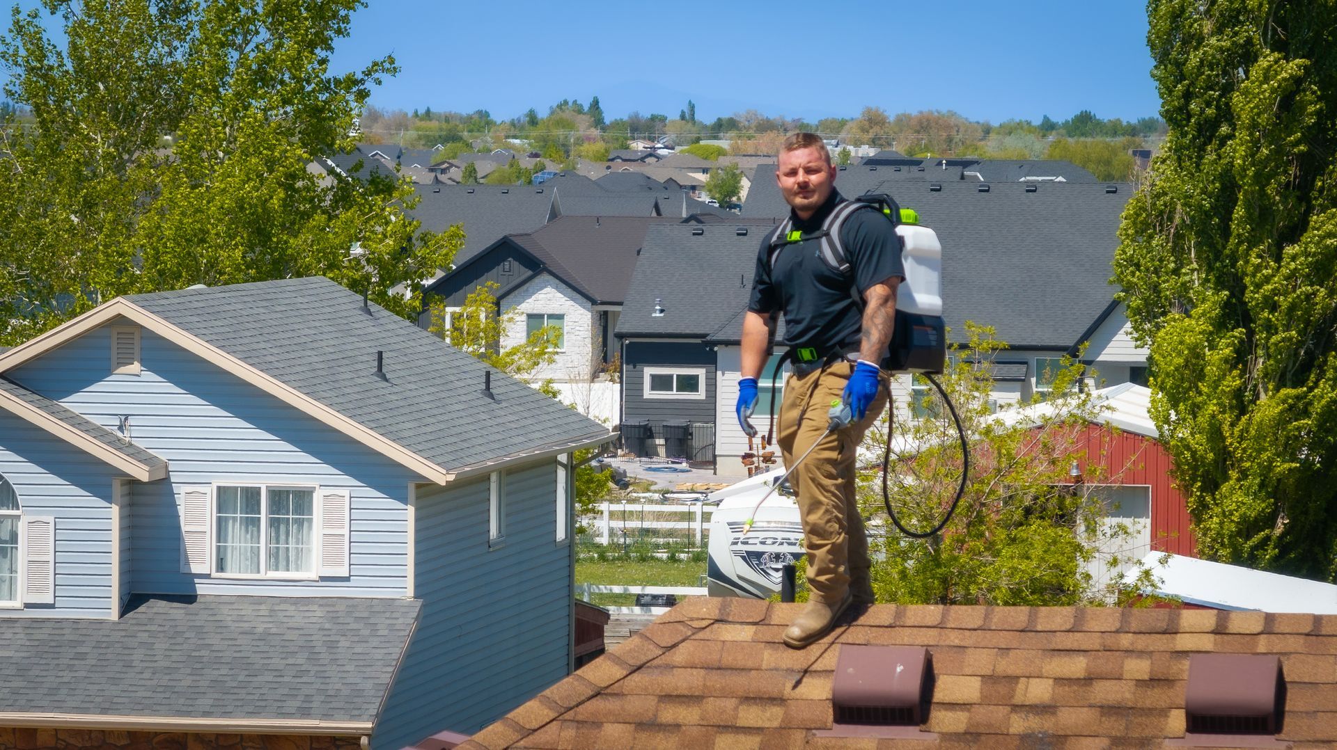 A man is standing on top of a roof spraying insecticide.