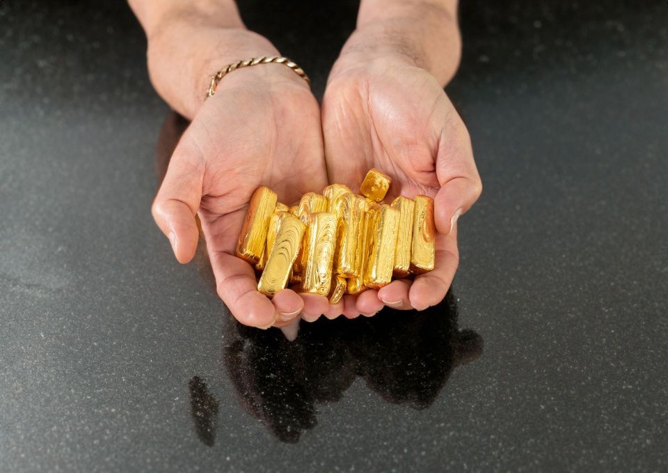 mani che tengono dei piccoli lingotti di oro
