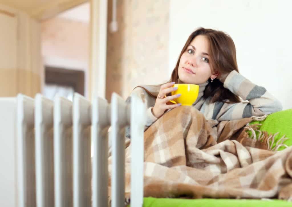 woman drinking from a mug on the couch near a radiator