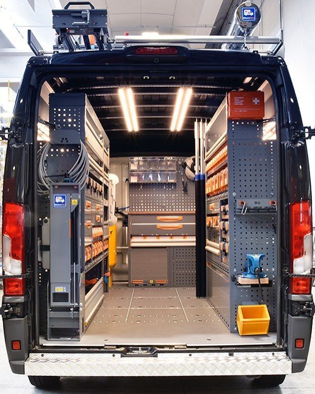 Interior de uma van de serviço com ferramentas e equipamentos organizados, iluminada por luzes de trabalho.