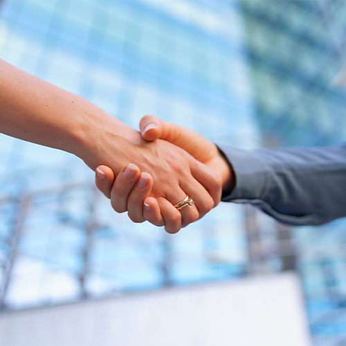 Duas mãos unidas em um aperto de mãos; ambiente de negócios, fundo desfocado de um prédio moderno.