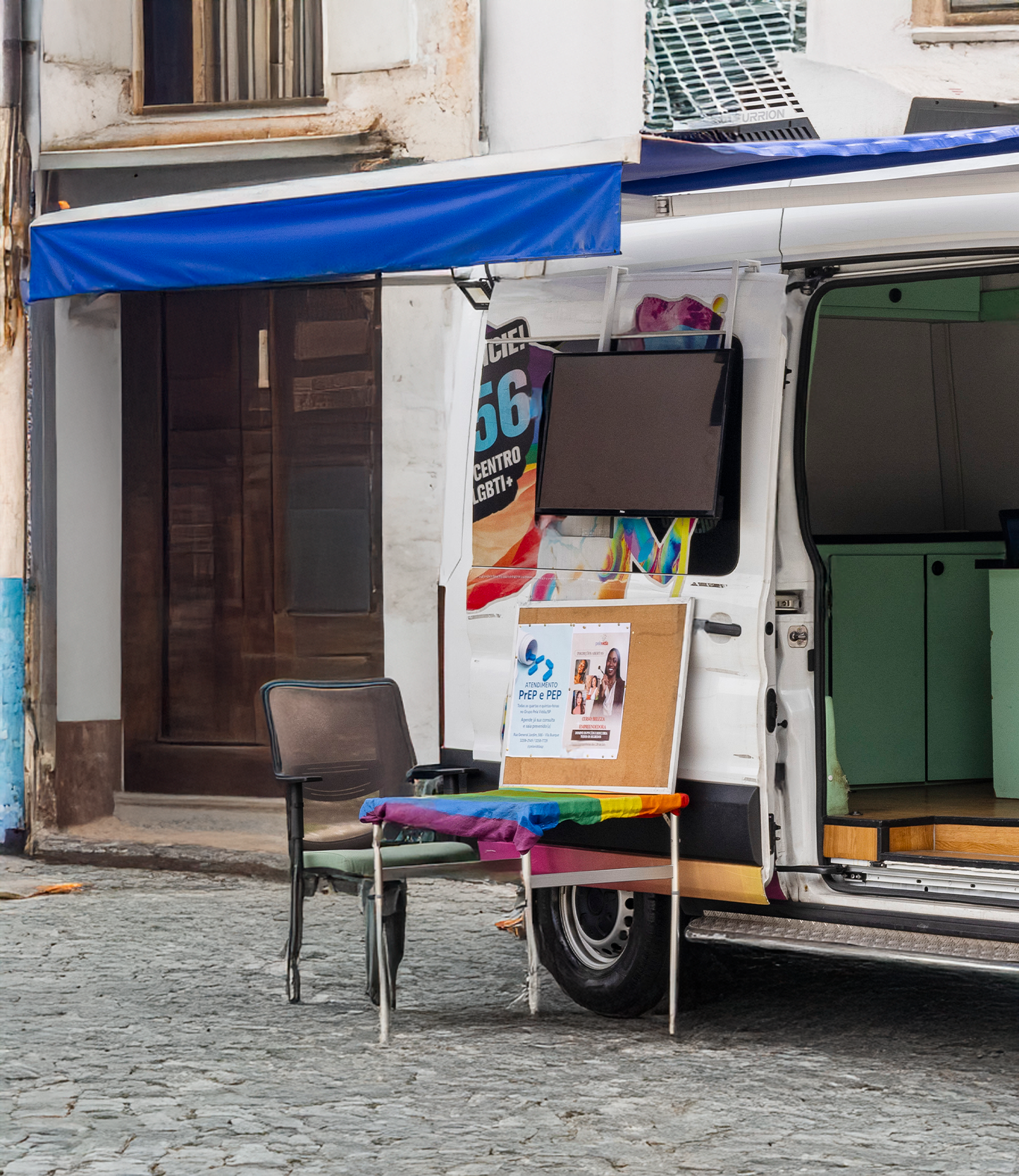 Van branca com traseira aberta exibindo mobiliário em rua de paralelepípedos.