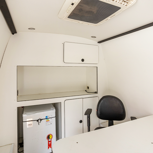 Interior branco de uma clínica médica móvel com geladeira, armários, mesa e cadeira de escritório.
