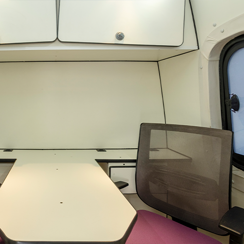 Interior de uma autocaravana com uma secretária, cadeira, armários e uma janela.