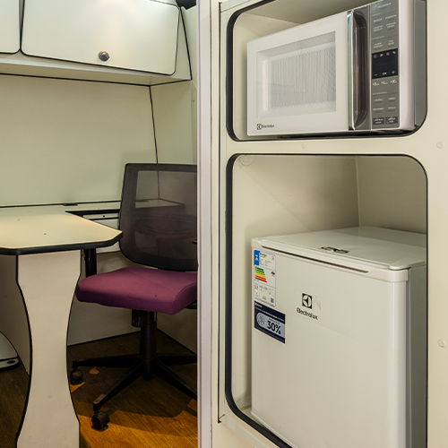 Interior de um pequeno escritório/sala de estar com micro-ondas, frigobar, mesa e cadeira.