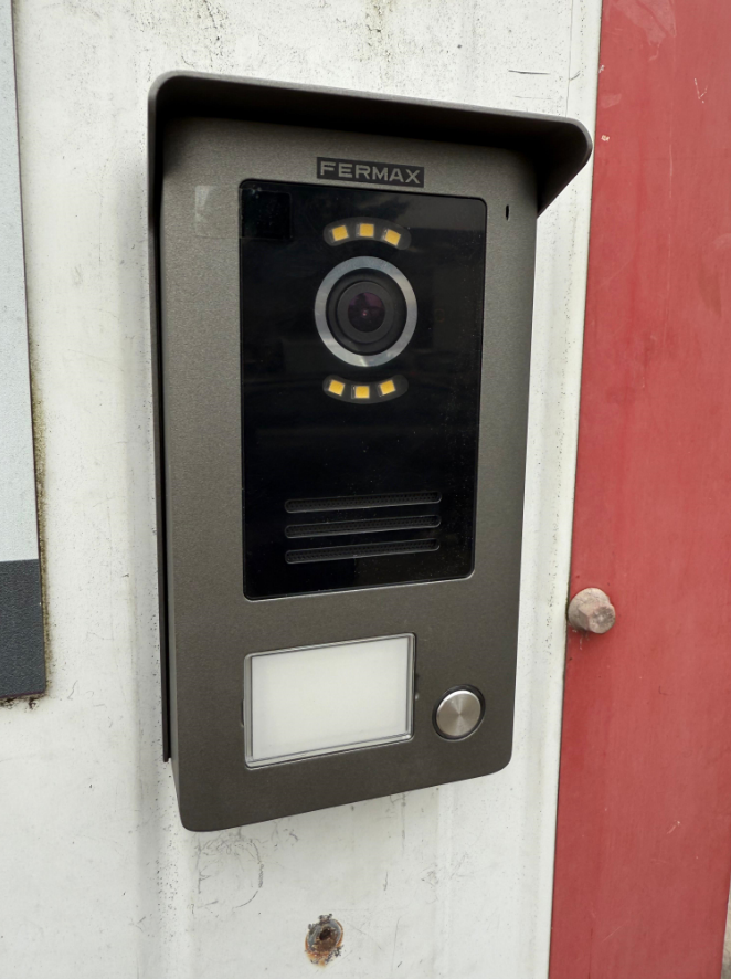 Une caméra est montée sur un mur blanc à côté d'une porte rouge.