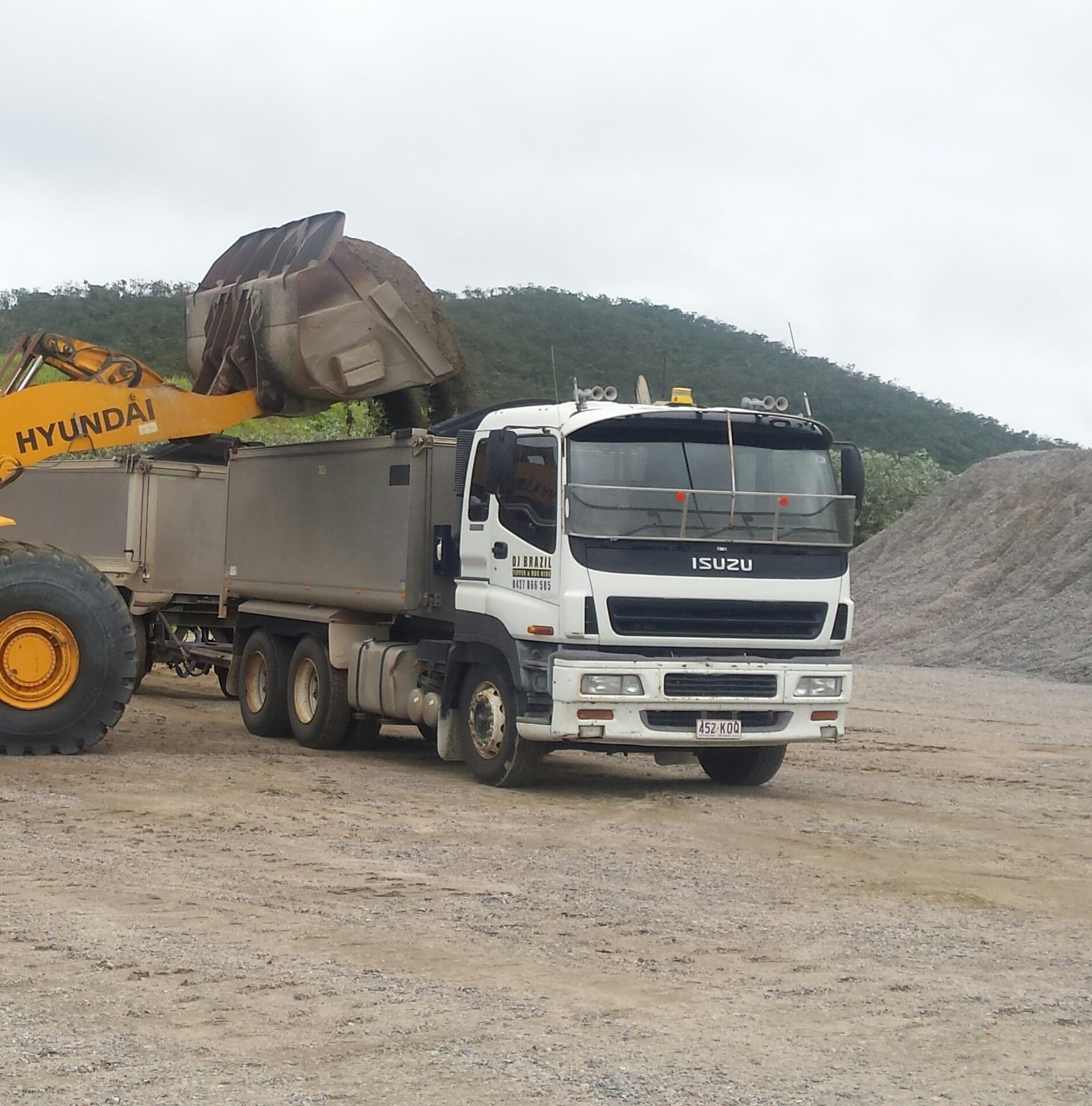 Excavator Loading a White Isuzu Dump Truck With Gravel — DJ Brazil Pty Ltd in Bowen, QLD