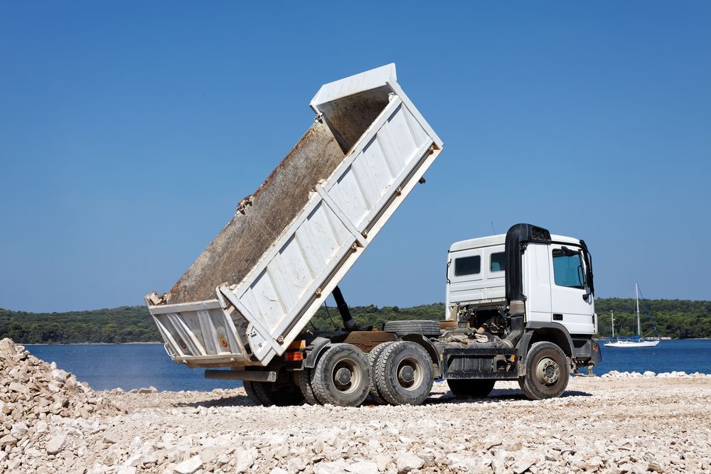 Red Dump Truck Unloading Brown Dirt on a Grassy Hillside — DJ Brazil Pty Ltd in Bowen, QLD