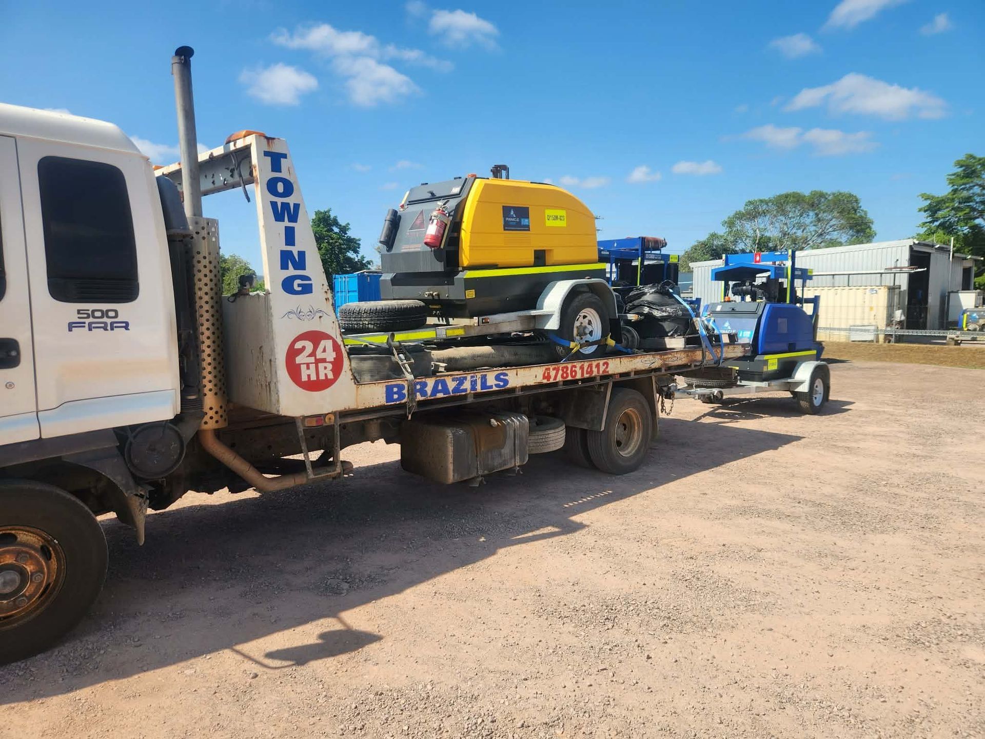 Tow truck hauling two pieces of equipment on a flatbed trailer, under a blue sky. . - DJ Brazil earthmoving, truck and tilt tray hire, Bowen QLD