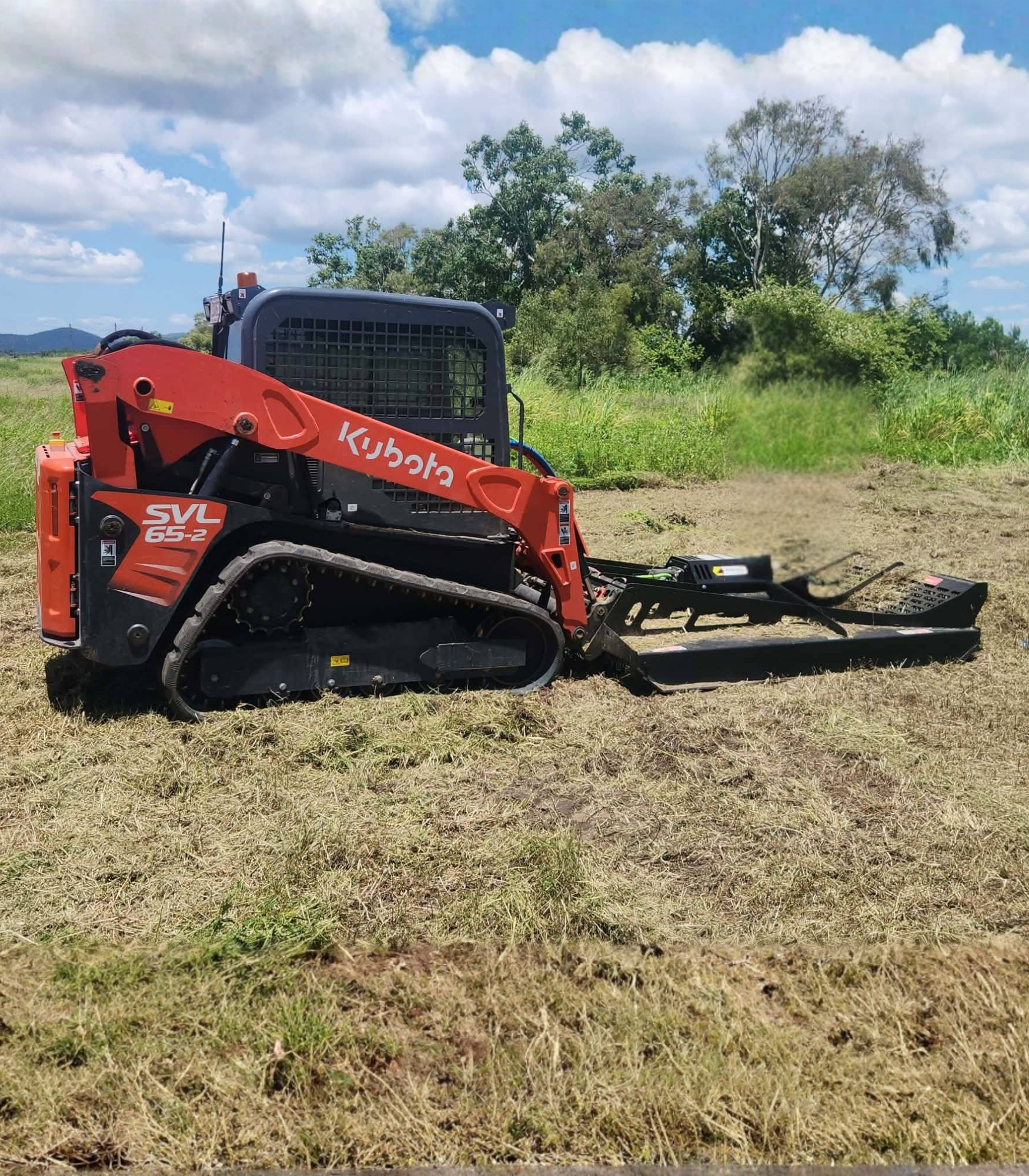 Orange Kubota track skid steer with brush cutter in a field. . - DJ Brazil earthmoving, truck and tilt tray hire, Bowen QLD