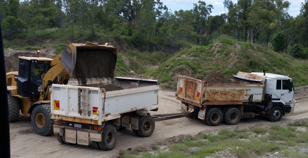 A Yellow Loader Dumping Dirt Into a White Trailer — DJ Brazil Pty Ltd in Bowen, QLD
