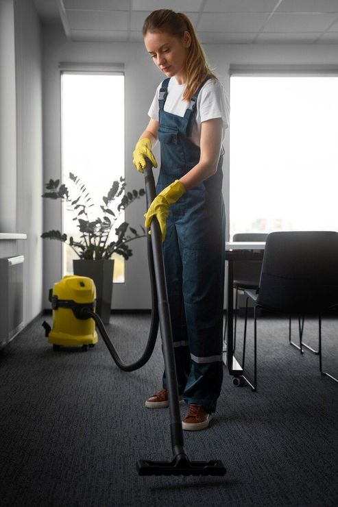 A woman is using a vacuum cleaner to clean the carpet in an office.