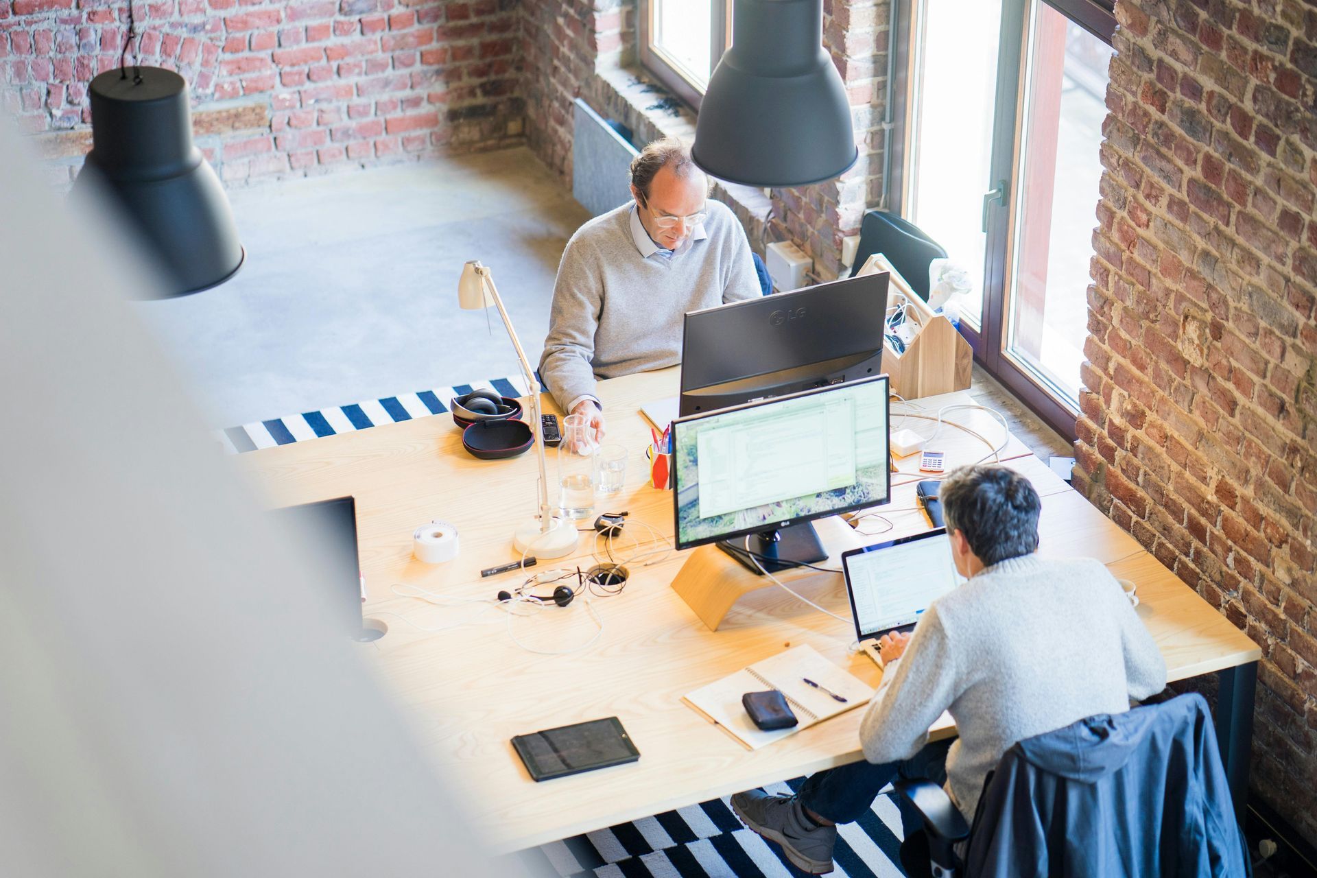 Two men are sitting at a desk in an office working on computers.
