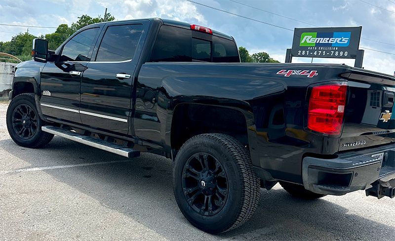 Black Chevrolet pickup truck parked near a business with a blue and green sign, side view.