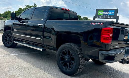 Black Chevrolet pickup truck parked near a business with a blue and green sign, side view.