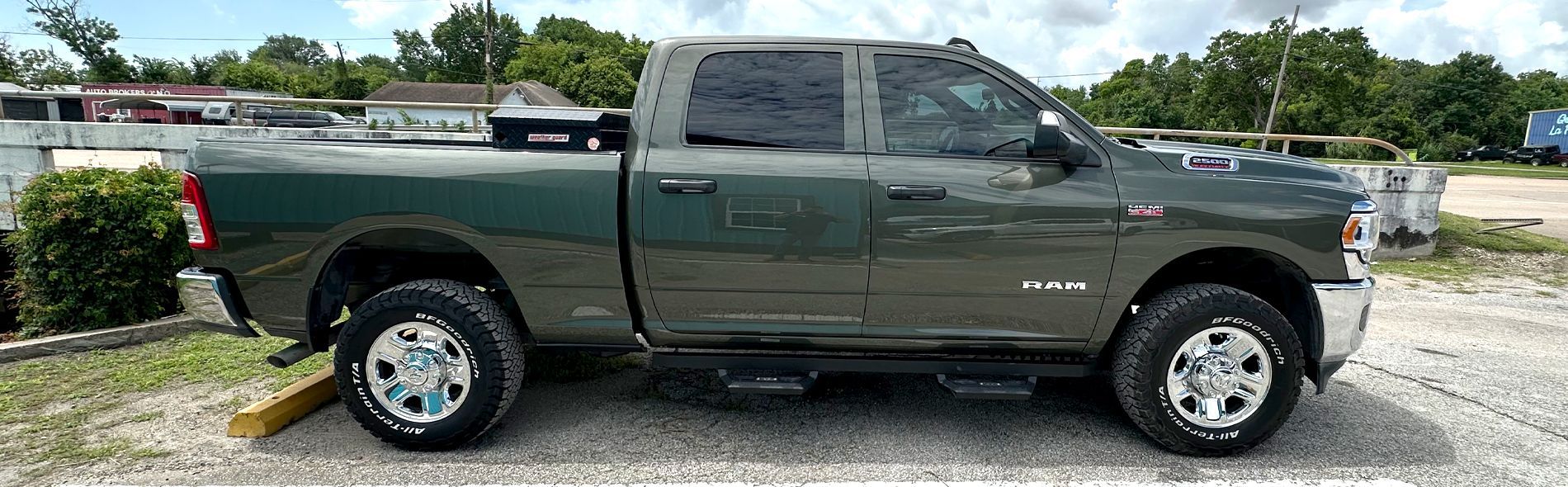 A dark green pickup truck parked on a gravel lot near vegetation.
