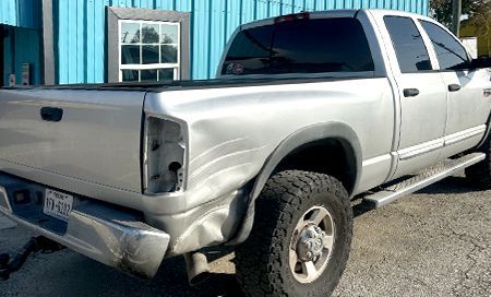 Silver pickup truck with a damaged rear end, parked outside a building.