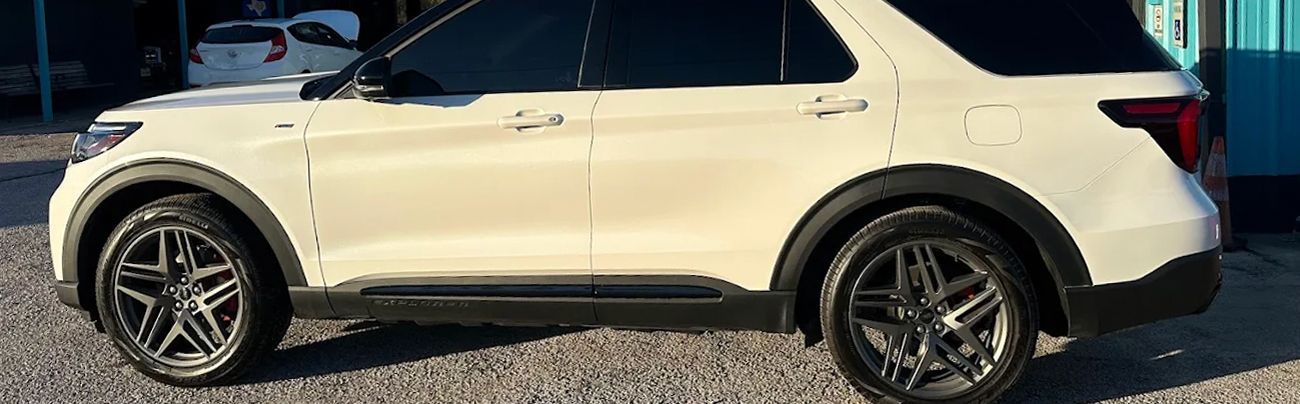 White Ford Explorer SUV with black wheels, parked outdoors on gravel.