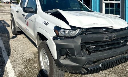 White pickup truck with front-end damage, likely from a collision. It is parked outside a building.