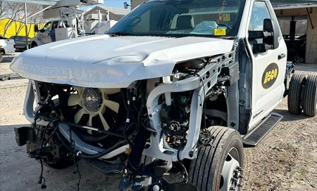 White pickup truck with front-end damage; hood crumpled, engine exposed.