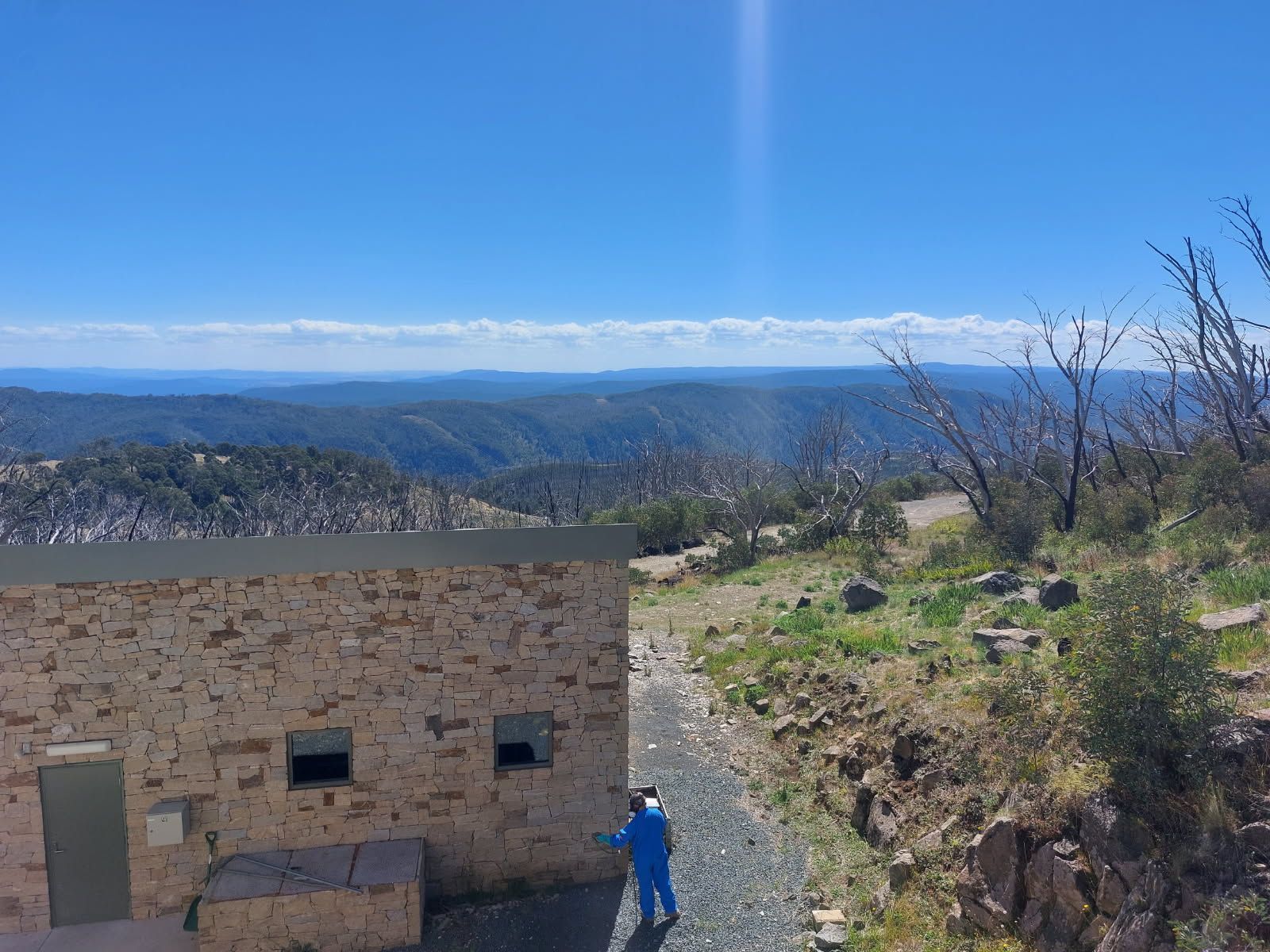 A Man in a Blue Jacket is Standing in Front of a Stone Building on Top of a Hill — Border Pest Control In Albury, NSW